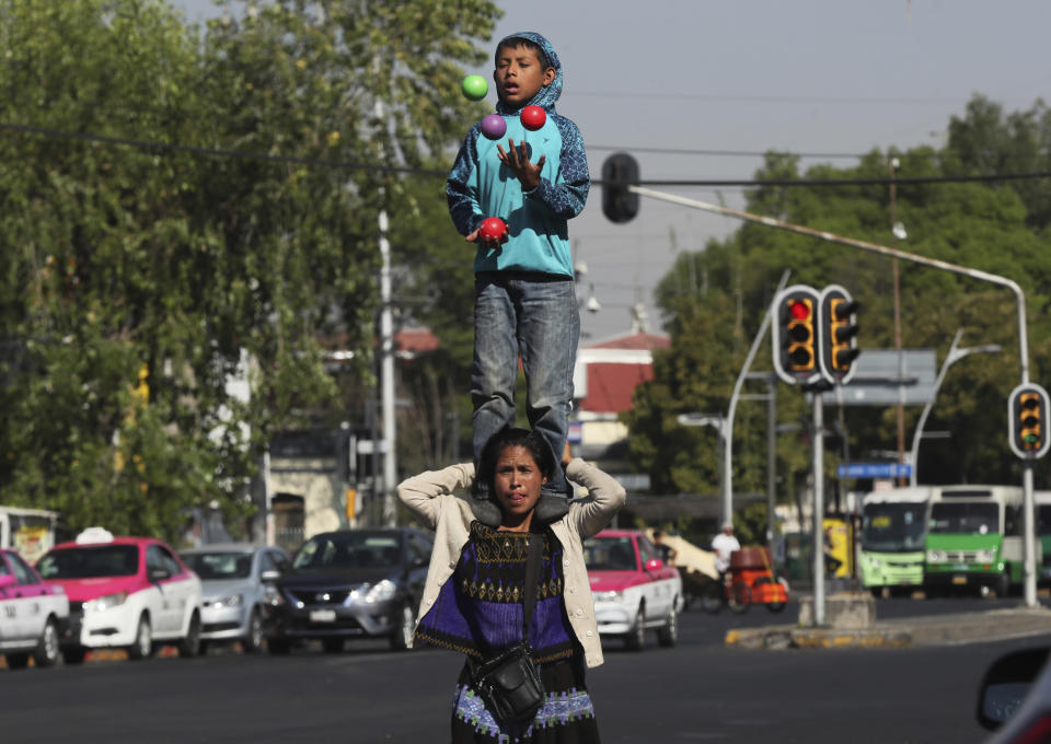 A woman holds a boy on her shoulders as they perform on a street in Mexico City, Monday, March 9, 2020. Thousands of women across Mexico went on strike after an unprecedented number of girls and women hit the streets to protest rampant gender violence on International Women's Day. (AP Photo/Fernando Llano)
