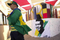 A fan walks past a portrait of Pelé displayed at a Brazilian fan party before the the World Cup round of 16 soccer match between Brazil and South Korea, in Doha, Dec. 5, 2022. The 82-year-old Pelé remained in a hospital in San Paulo recovering from a respiratory infection that was aggravated by COVID-19, but the news coming from Brazil early Monday was good. (AP Photo/Ashley Landis)