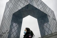 A woman wearing a face mask to protect against COVID-19 walks along a street in the central business district in Beijing, Thursday, Dec. 23, 2021. China has ordered the lockdown of as many as 13 million people in neighborhoods and workplaces in the northern city of Xi'an following a spike in coronavirus cases, setting off panic buying just weeks before the country hosts the Winter Olympics. (AP Photo/Mark Schiefelbein)