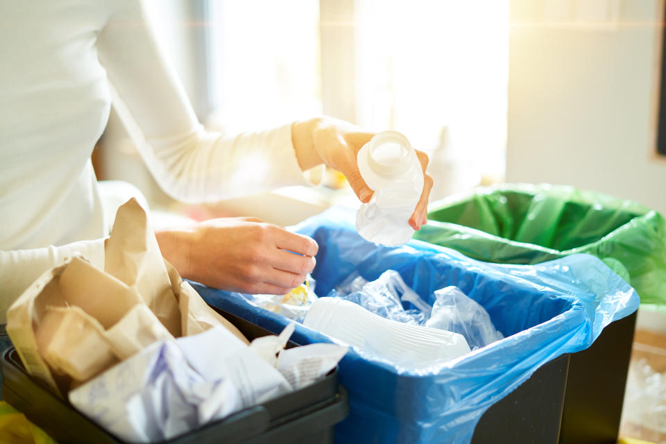 Close up view of hands of young woman sorting garbage in kitchen.