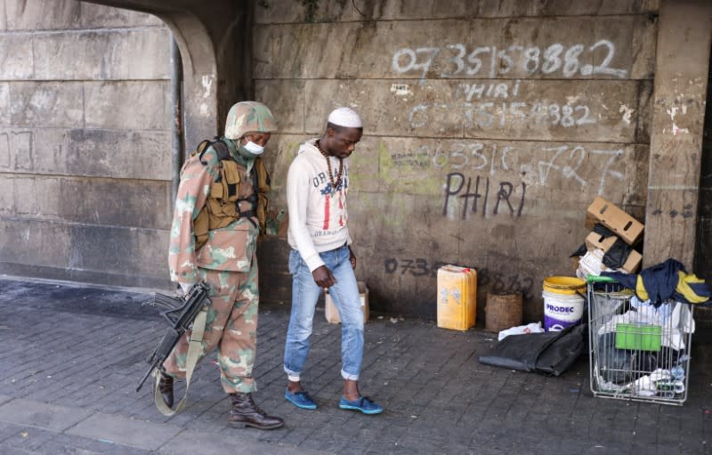 A member of the South African National Defense Force escorts a homeless men in Johannesburg