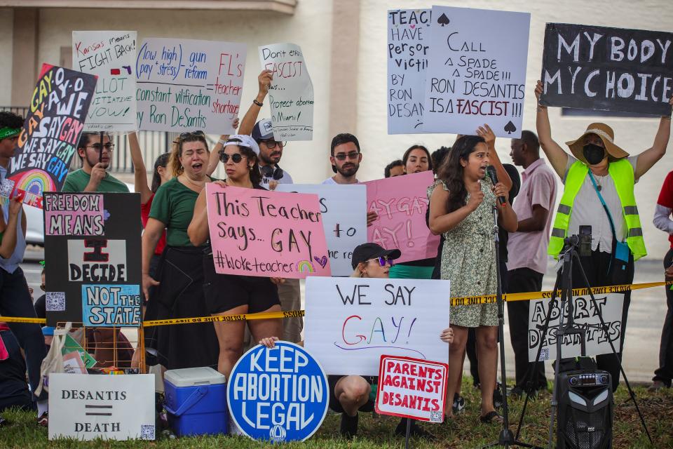 Protesters stand in front of a building holding signs reading: DeSantis = Death and Parents Against DeSantis.