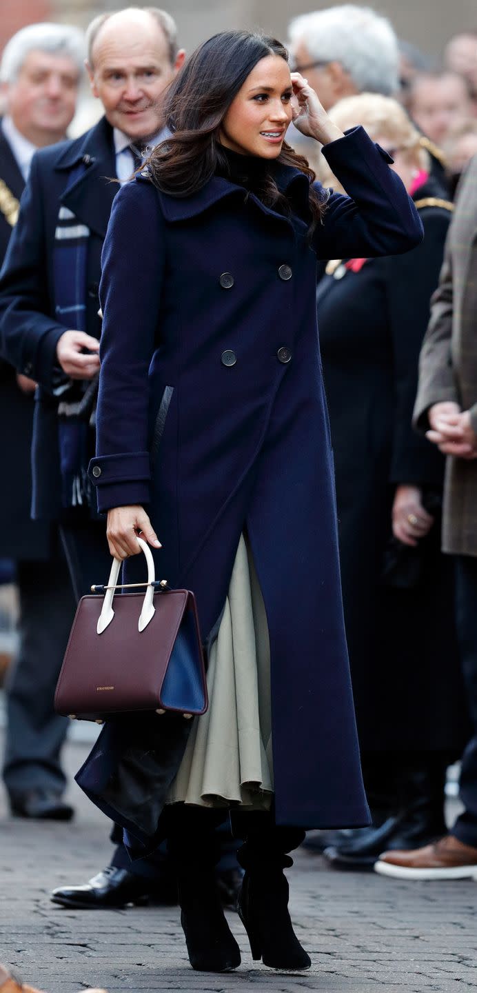 <p>Meghan attended her first public appearance with Prince Harry in Nottingham wearing an all-British/Amercian fashion ensemble comprising of a double-breasted Mackage navy coat, Joseph skirt and carried a burgundy and navy blue Strathberry handbag. </p>