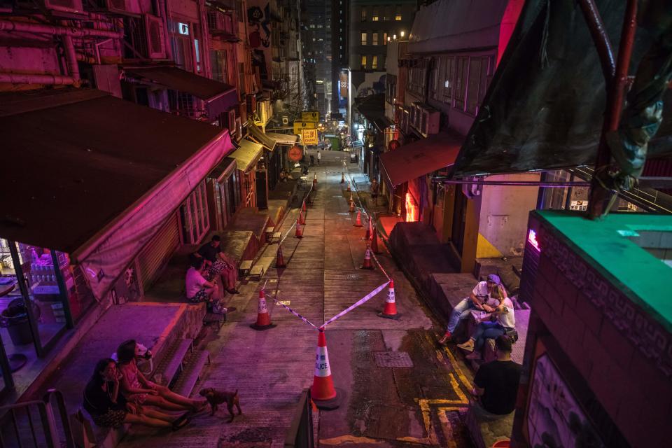 TOPSHOT - This photo taken on March 18, 2022 shows people sitting on a street cordoned off by police with bars and restaurants closed due to Covid-19 coronavirus restrictions in Hong Kong. (Photo by DALE DE LA REY / AFP) (Photo by DALE DE LA REY/AFP via Getty Images)