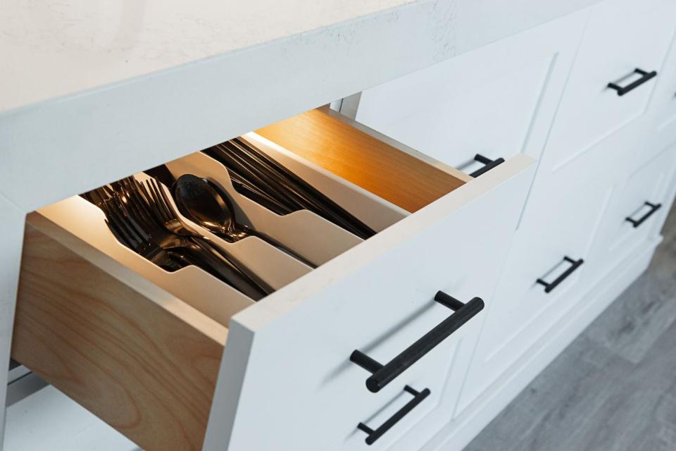 A close up of black cabinet hardware on an open kitchen drawer filled with utensils.