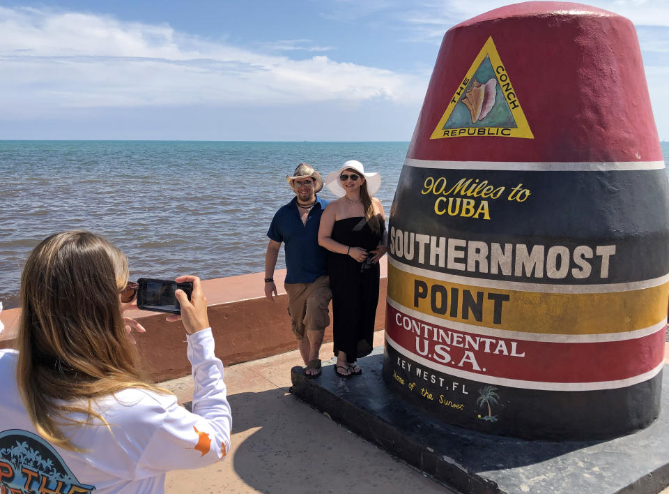 In this photo provided by the Florida Keys News Bureau, Kim Stamps, left, photographs Michigan newlyweds Tyler Gillet, middle, and Ashley Gillet, right, by the Southernmost Point marker Saturday, Aug. 31, 2019, in Key West, Fla. After significant changes in the forecast track for Hurricane Dorian, that removed the Florida Keys from the forecast cone Saturday, local officials encouraged visitation to the island chain. (Carol Tedesco/Florida Keys News Bureau via AP)