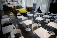 A man sits in front of a Porsche 911 sports car on display at its dealership during a news conference in Seoul