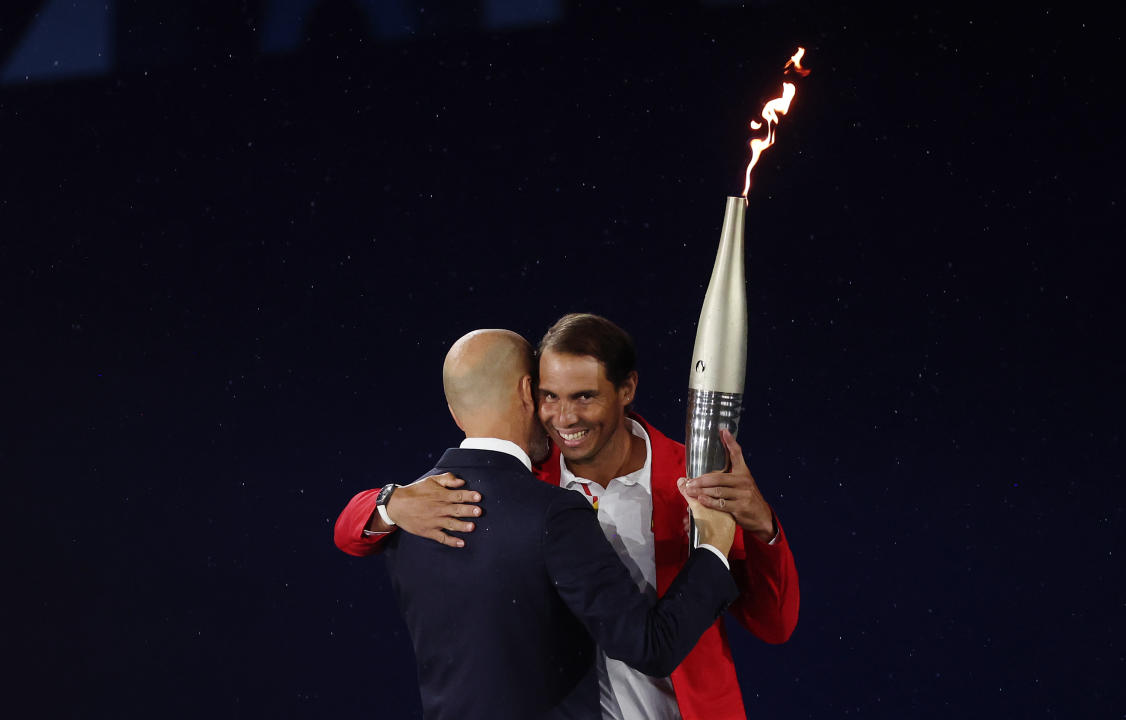 PARIS, FRANCE - JULY 26: Former French Footballer Zinedine Zidane embraces Tennis Player Rafael Nadal of Team Spain, 14 Time French Open Winner, as they exchange the Olympic Torch during the opening ceremony of the Olympic Games Paris 2024 on July 26, 2024 in Paris, France. (Photo by Matthew Stockman/Getty Images)