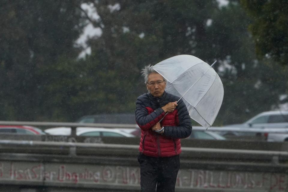 A man uses an umbrella to shield from the wind and rain in Oakland, Calif., Tuesday, March 21, 2023. (