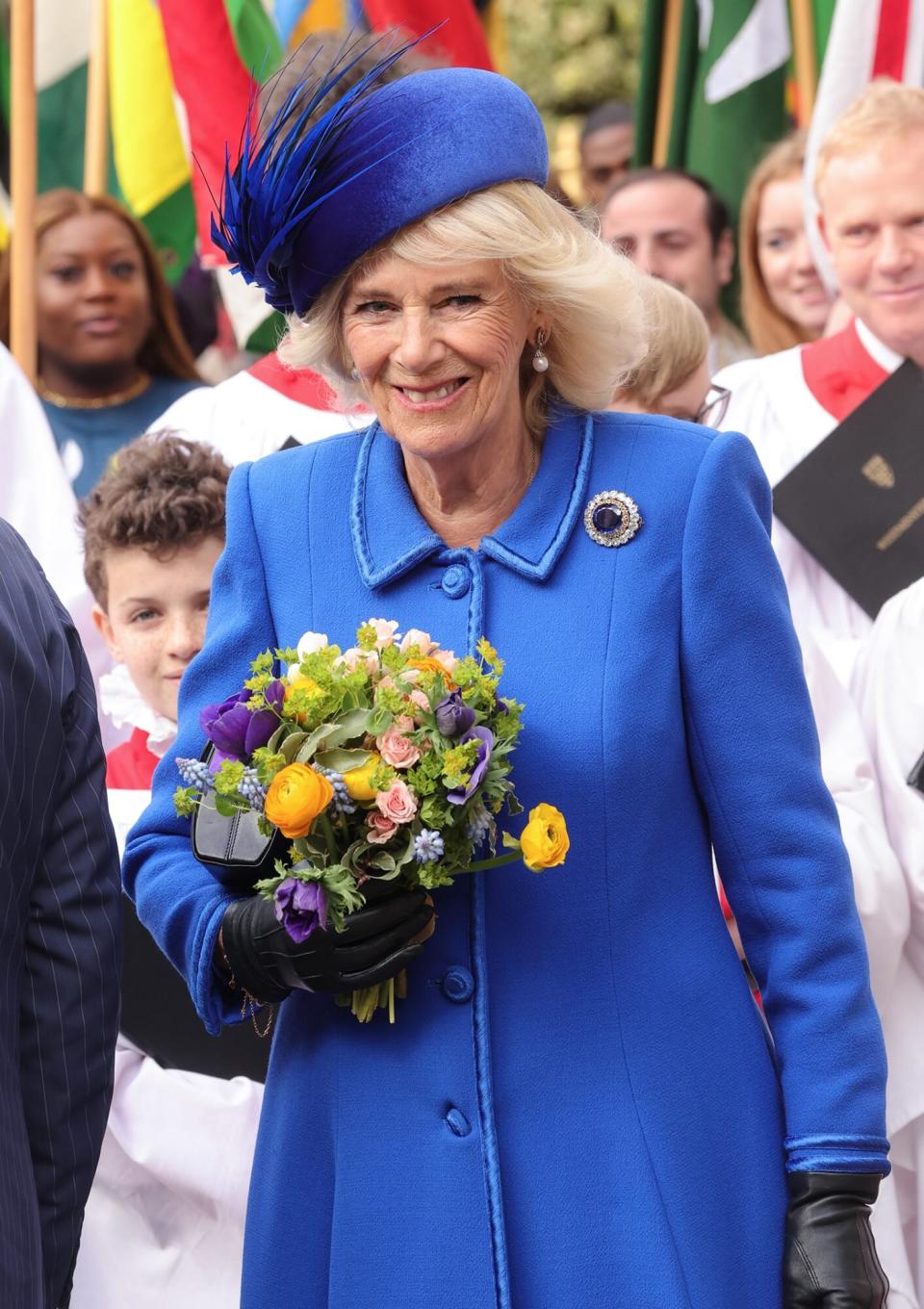 Camilla, Queen Consort holds a bouquet of flowers and smiles as she departs the 2023 Commonwealth Day Service at Westminster Abbey
