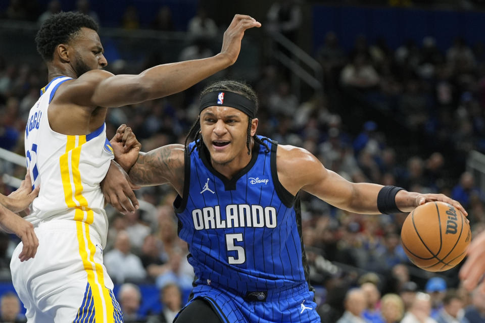 Orlando Magic forward Paolo Banchero (5) tries to get past Golden State Warriors forward Andrew Wiggins during the first half of an NBA basketball game Wednesday, March 27, 2024, in Orlando, Fla. (AP Photo/John Raoux)