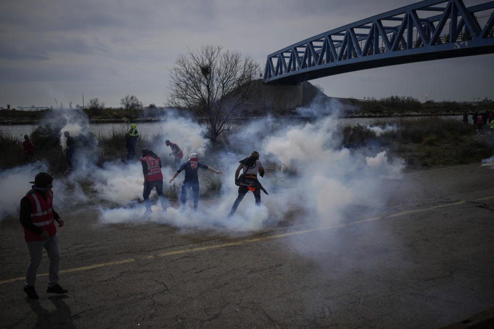 Oil workers stand in the tear gas thrown by riot police as they block the access to an oil depot in Fos-sur-Mer, southern France, Tuesday, March 21, 2023. The bill pushed through by President Emmanuel Macron without lawmakers' approval still faces a review by the Constitutional Council before it can be signed into law. Meanwhile, oil shipments in the country were disrupted amid strikes at several refineries in western and southern France. (AP Photo/Daniel Cole)