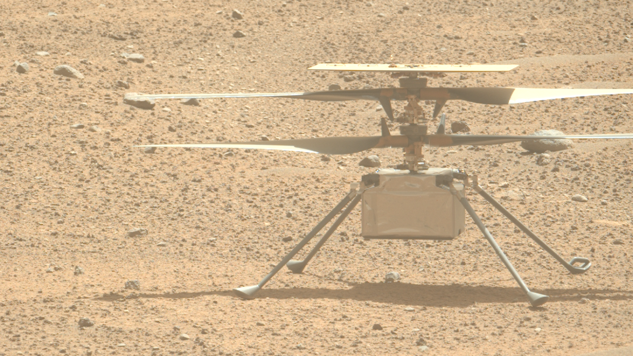  Closeup of a four-rotor drone sitting on pebbly red dirt. 