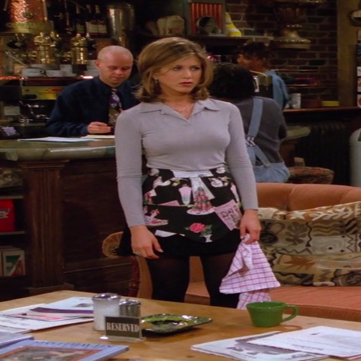 Rachel wearing small booties, tights, a skirt, an apron, and a long-sleeve shirt with a collar like a blazer