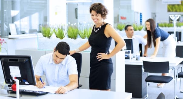 Two business persons working at office desk with colleagues in the back