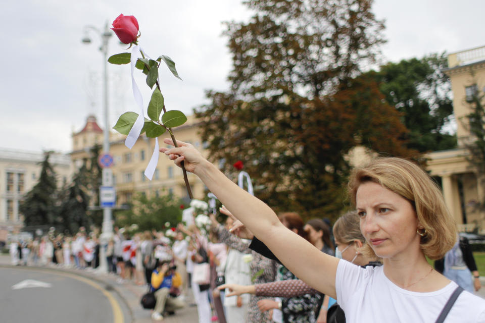 Belarusian opposition supporters hold flowers and flash victory signs during a protest in Victory Square in Minsk, Belarus, Thursday, Aug. 20, 2020. Demonstrators are taking to the streets of the Belarusian capital and other cities, keeping up their push for the resignation of the nation's authoritarian leader. President Alexander Lukashenko has extended his 26-year rule in a vote the opposition saw as rigged. (AP Photo/Sergei Grits)