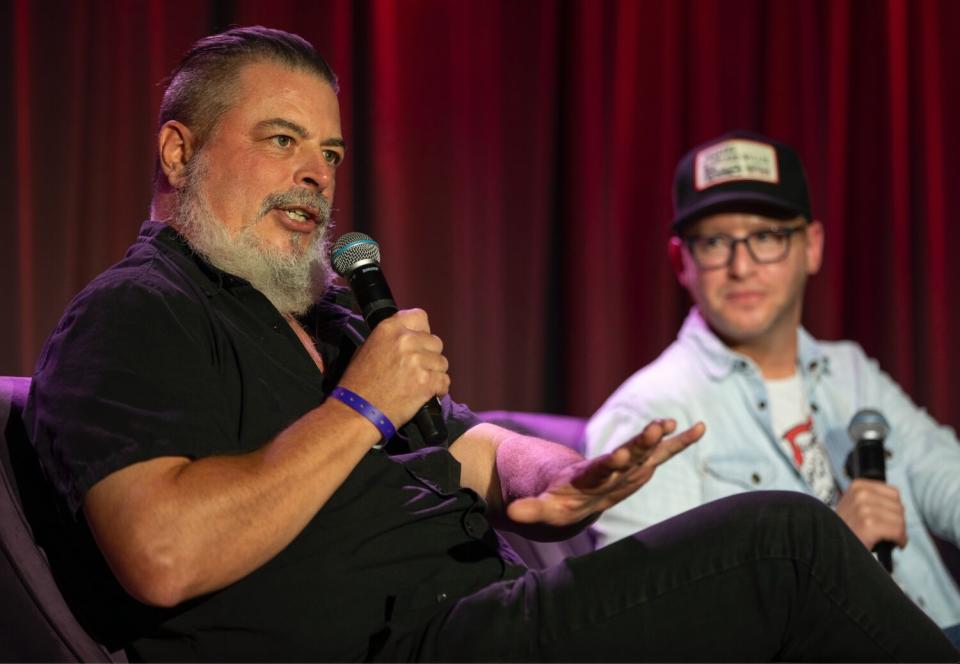 Two men seated onstage hold microphones and answer audience questions.