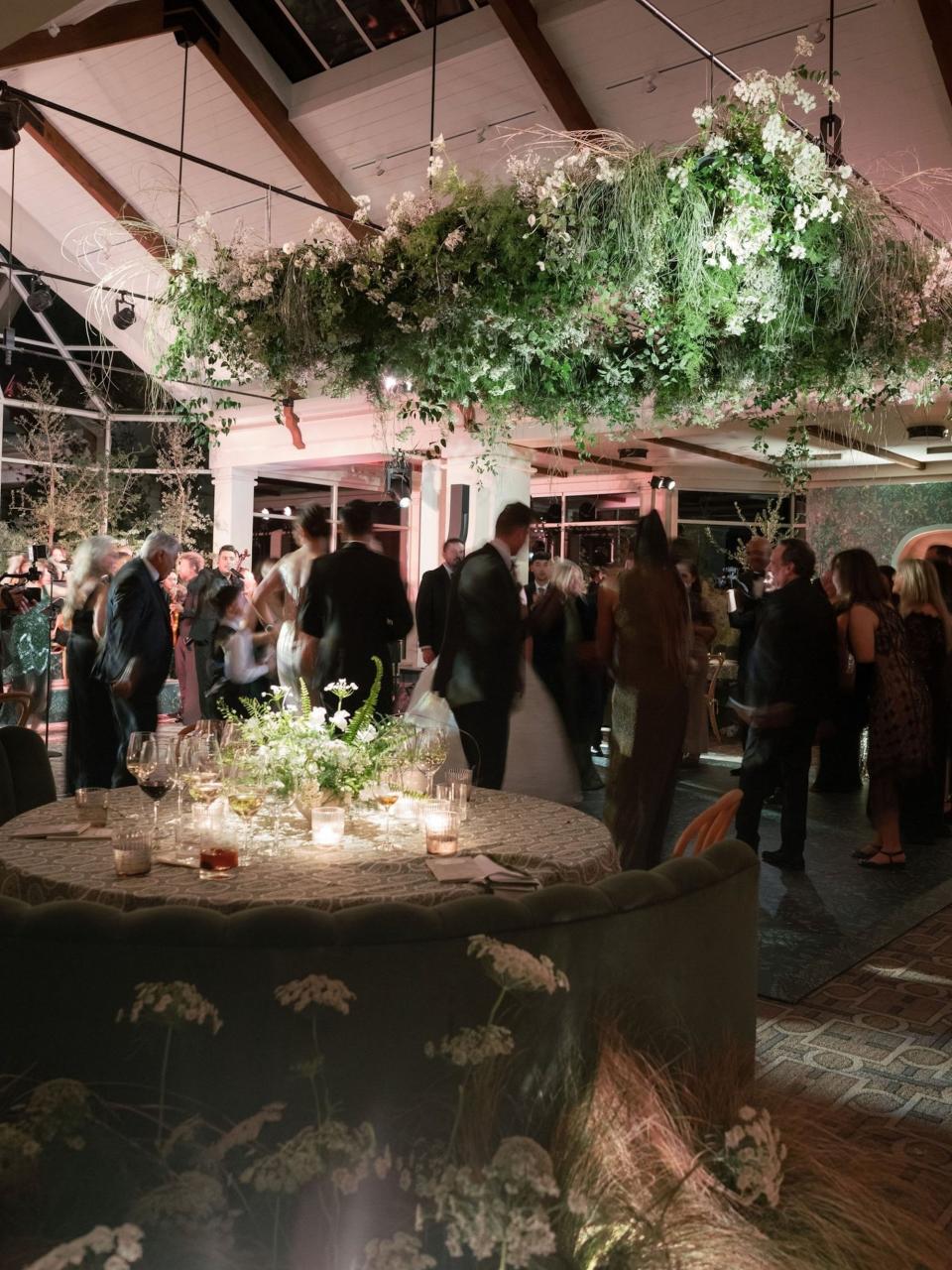 A wedding reception where people dance under a massive floral arrangement.