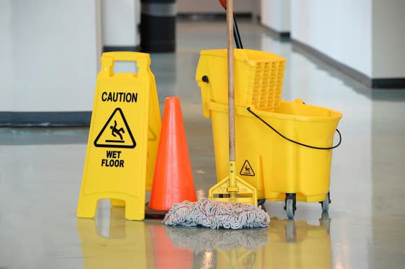Yellow mop and caution sign next to a yellow bucket, with an orange cone in the middle