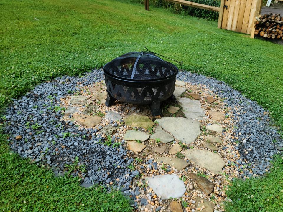 A black firepit surrounded by rocks and grass.