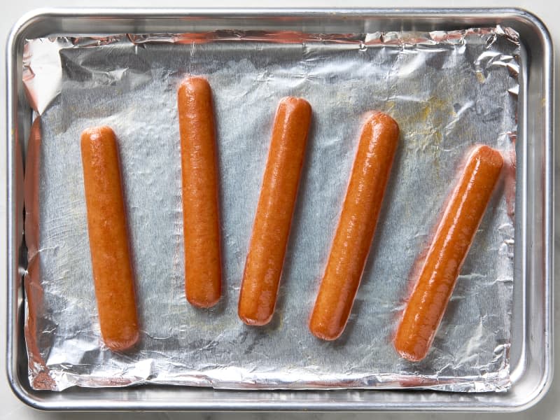 overhead photo of hot dogs cooked in the oven on a foil lined sheet pan