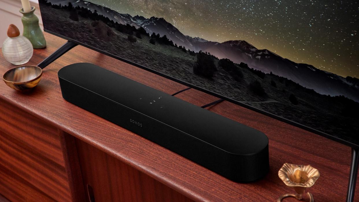  A black Sonos Beam Gen 2 in front of a TV on top of a wooden rack. 