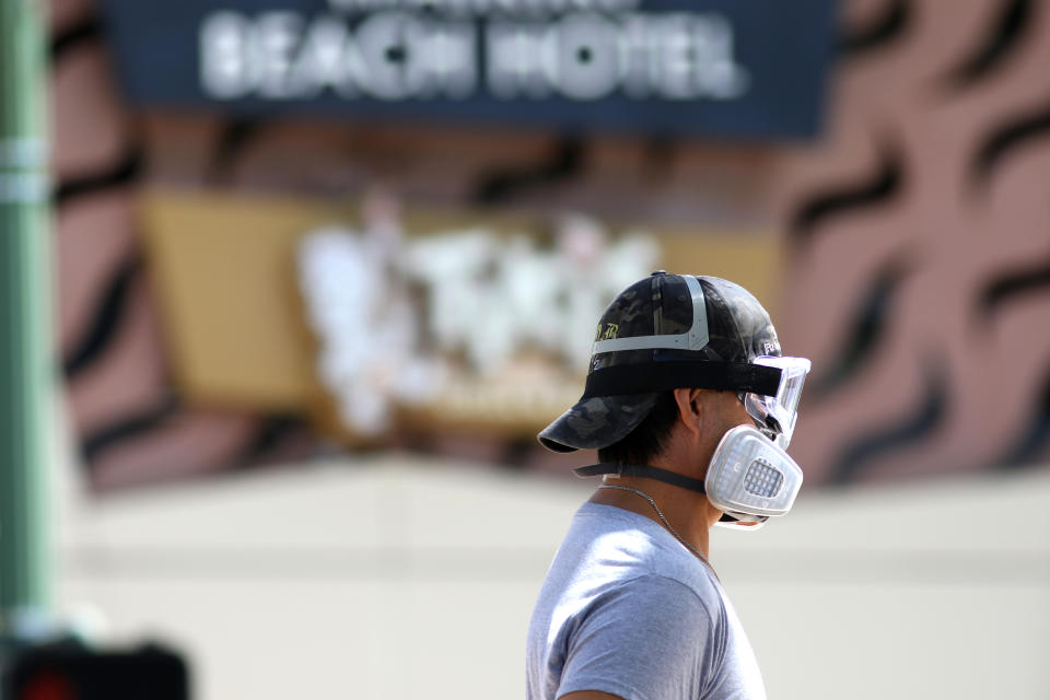 A man wears goggles and a mask as he walks a dog along Waikiki Beach in Honolulu on Saturday, March 28, 2020. Like many cities across the world, Honolulu came to an eerie standstill this weekend as the coronavirus pandemic spread throughout the islands. But Hawaii officials went beyond the standard stay-at-home orders and effectively flipped the switch on the state's tourism-fueled economic engine in a bid to slow the spread of the virus. As of Thursday, anyone arriving in Hawaii must undergo a mandatory 14-day self-quarantine. The unprecedented move dramatically reduced the number of people on beaches, in city parks and on country roads where many people rely on tourism to pay for the high cost of living in Hawaii. (AP Photo/Caleb Jones)
