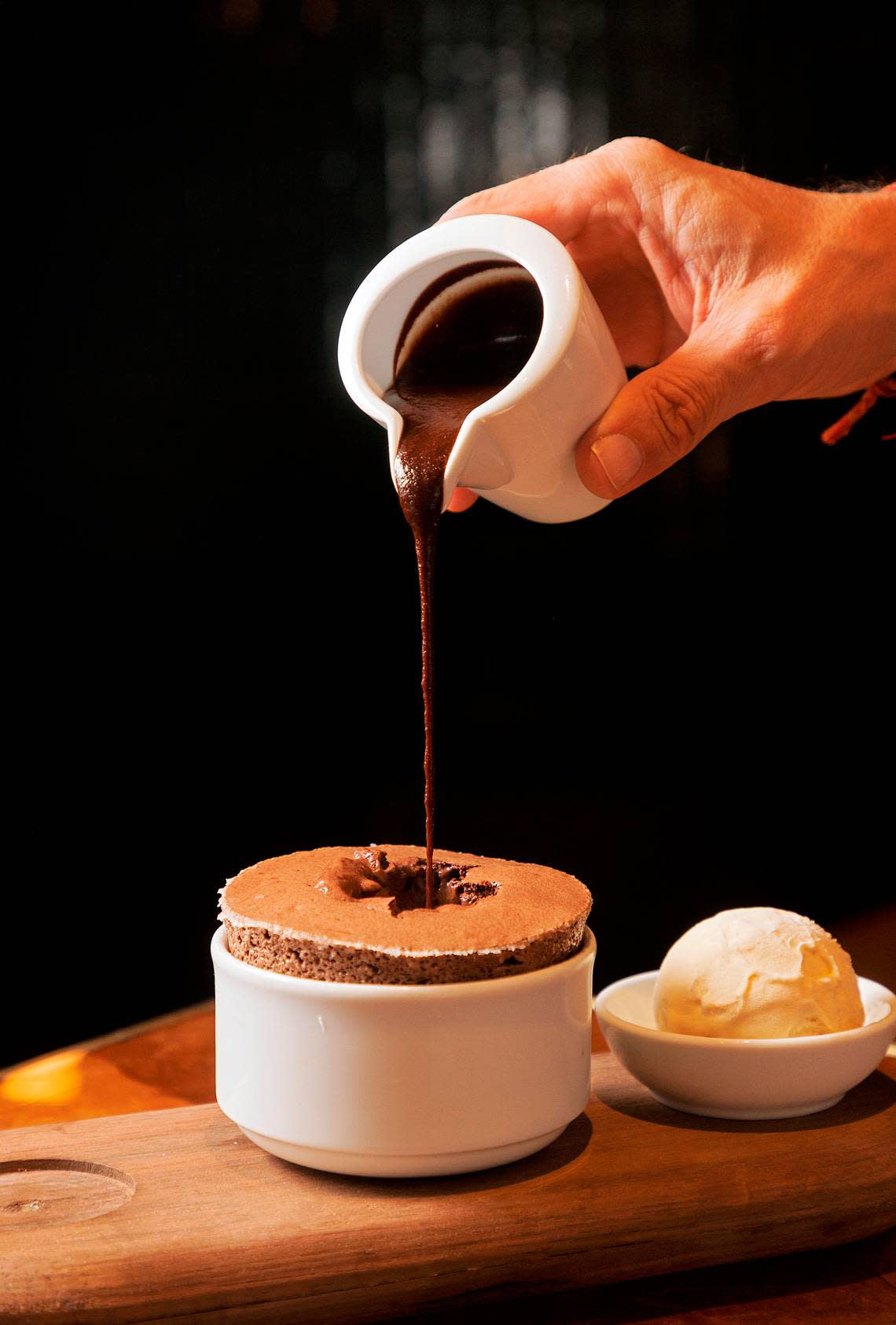 Hot fudge is poured into a hot chocolate soufflé, served alongside bourbon caramel ice cream at Nanas on Wednesday, Nov. 22, 2023, in Durham, N.C.