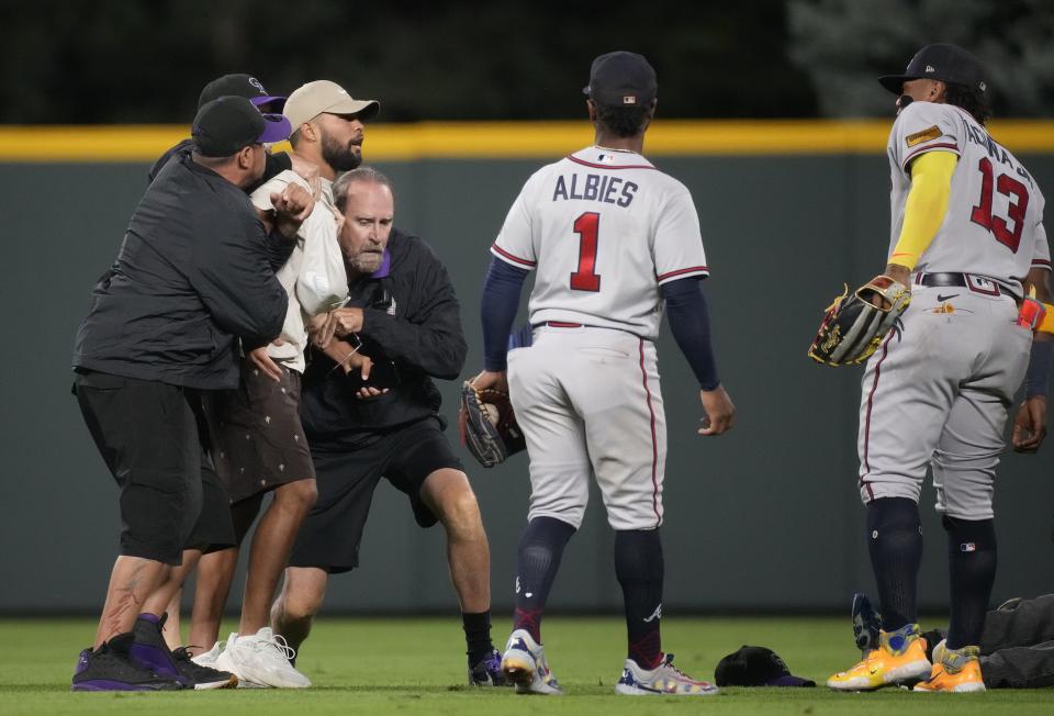 Field guards hold back a fan as he exchanges words with Atlanta Braves right fielder Ronald Acuna Jr., right, as second baseman Ozzie Albies (1) looks on in the seventh inning of a baseball game against the Colorado Rockies, Monday, Aug. 28, 2023, in Denver. (AP Photo/David Zalubowski)