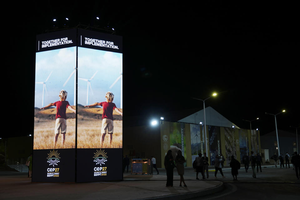 FILE - People walk past image of wind turbines at the COP27 U.N. Climate Summit, Tuesday, Nov. 8, 2022, in Sharm el-Sheikh, Egypt. (AP Photo/Peter Dejong, File)