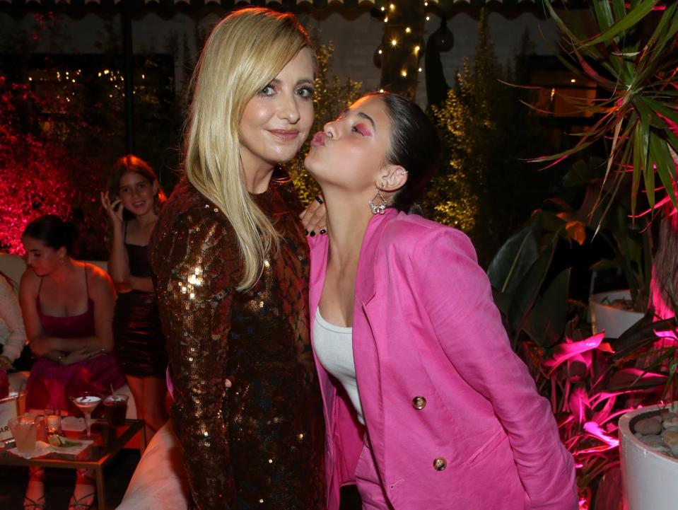 Sarah Michelle Gellar, in a sparkly long-sleeved mini dress, smiles at the camera while her daughter Charlotte Prinze, in a pink suit with white sneakers, leans in for a kiss.
