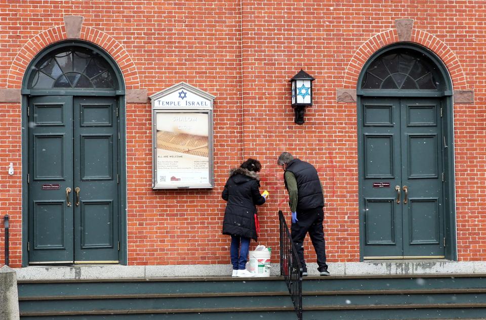 People work to remove a swastika from Temple Israel in Portsmouth Tuesday, Feb. 21, 2023. It was one of numerous buildings in the city hit with hate symbols overnight.