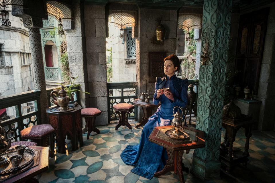 Moiraine sits on a balcony in a blue dress drinking tea in The Wheel of Time