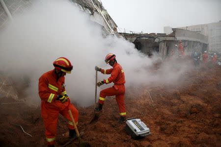 Firefighters search for survivors as smoke rises from a damaged building at the site of a landslide at an industrial park in Shenzhen, Guangzhou, China, December 20, 2015. REUTERS/Tyrone Siu