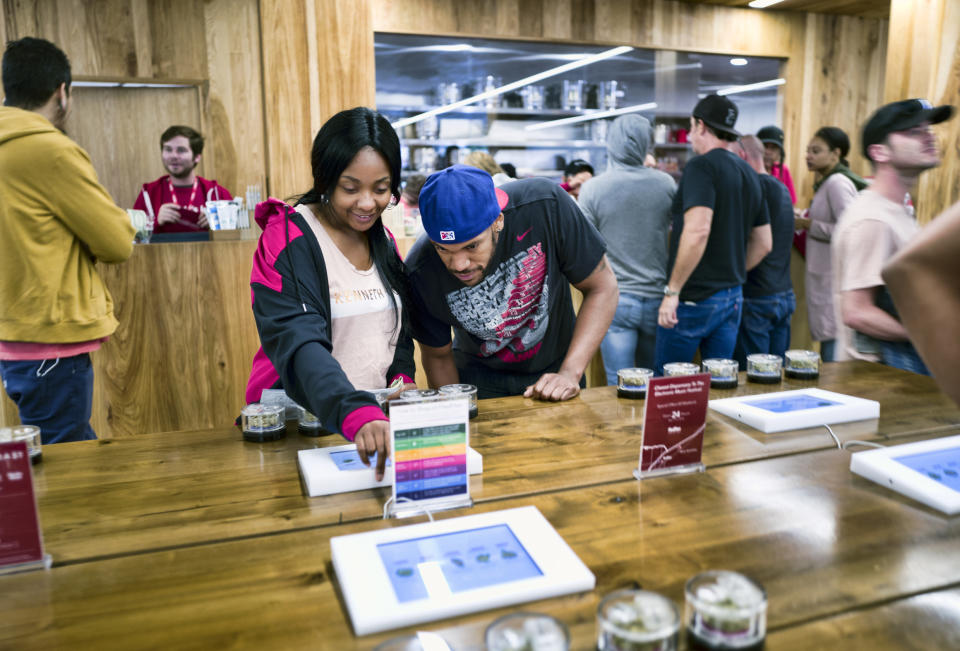 FILE - In this May 19, 2018 photo tourists Randy Wilkie and Keya Cole from Buffalo, New York, check out the offerings of cannabis at one of the MedMen cannabis dispensaries in Los Angeles, prior to boarding the Green Line Trips bus tour. California's struggling legal cannabis industry is expected to grow next year to $3.1 billion, but it remains far outmatched by the state's thriving illegal market. A report released Thursday, Aug. 15, 2019, finds consumers are spending roughly $3 in the state's underground pot economy for every $1 in the legal one. (AP Photo/Richard Vogel,File)