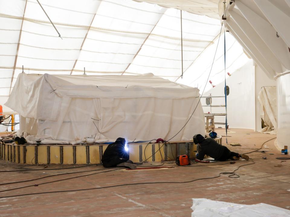 An indoor-outdoor space under construction with scaffolding on Royal Caribbean's Icon of the Seas . People are welding.