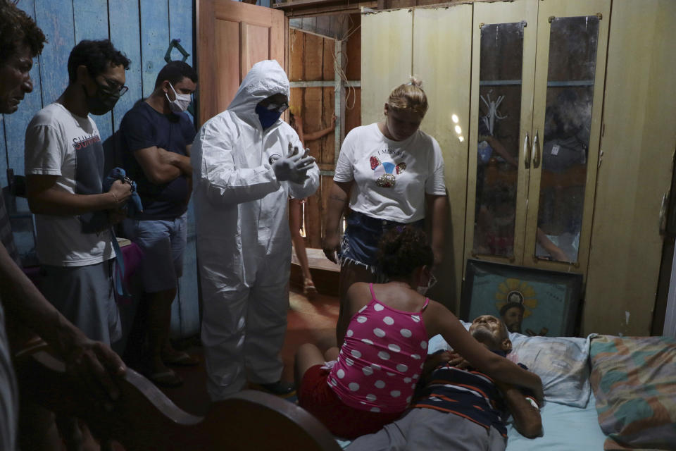 The body Raimundo Costa do Nascimento, 86, lies on a bed as the family mourns and a funeral worker in protection gear gets ready to pick up the body, amid the new coronavirus pandemic, at his home in Sao Jorge, Manaus, Brazil, Thursday, April 30, 2020. According to the family, Costa do Nascimento died of pneumonia and had to wait 10 hours for funerary services to come pick up his body. (AP Photo/Edmar Barros)