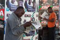 Men read newspapers in front of electoral campaign posters in Lagos March 30, 2015. REUTERS/Joe Penney