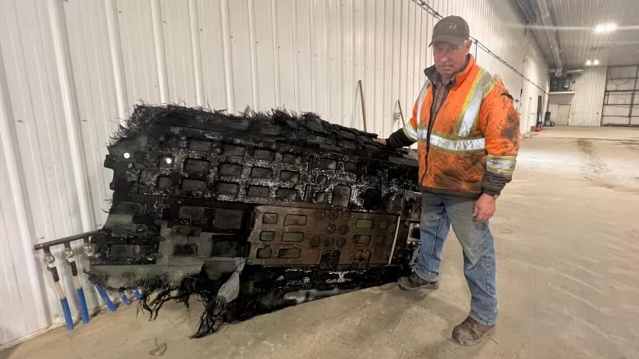  A person standing beside a very large piece of debris. the debris is charred and roughly the same width as a person's height. 