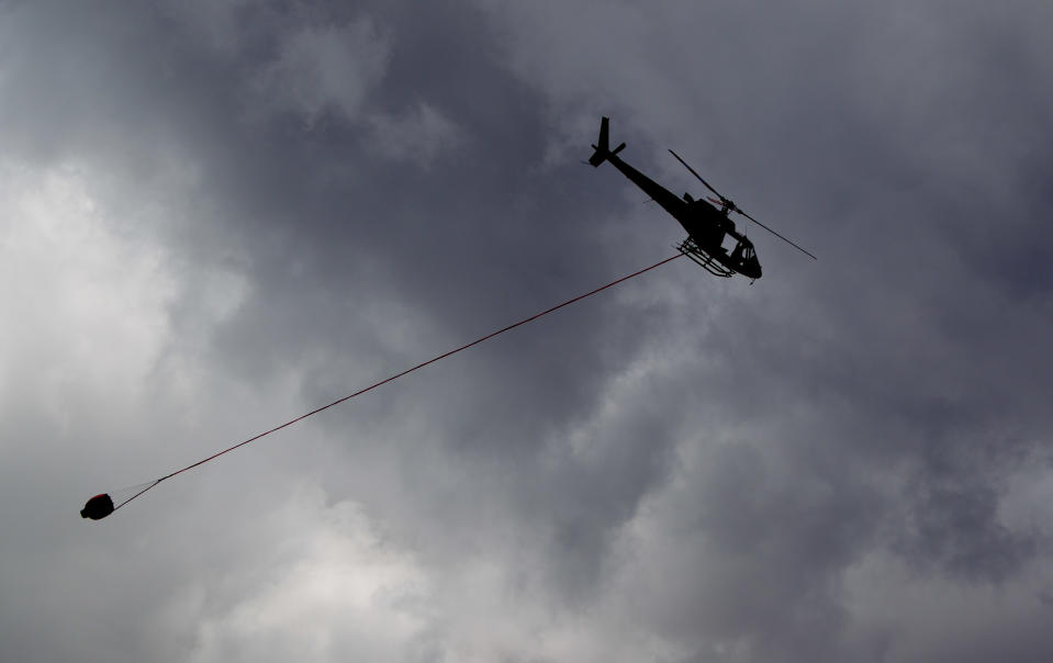 A helicopter from the Lady Lori charter company working in collaboration with the Kenyan Wildlife Service carries water to douse the flames of forest fires burning across the slopes of Mount Kenya, the second-highest peak in Africa at 5,199 meters (17,057 feet), in Kenya Tuesday, March 20, 2012. Fires that have been raging across Mount Kenya may have been set by poachers trying to create a diversion from their illegal attacks on animals, a wildlife official said Tuesday. (AP Photo/Ben Curtis)