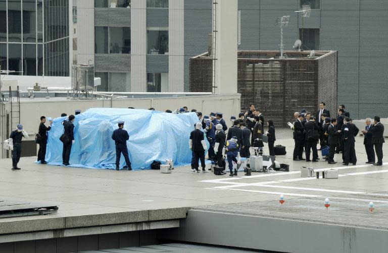 Police officers cover with a blue sheet and inspect a small drone, found on the roof of the Japanese prime minister's official residence in Tokyo, on April 22, 2015
