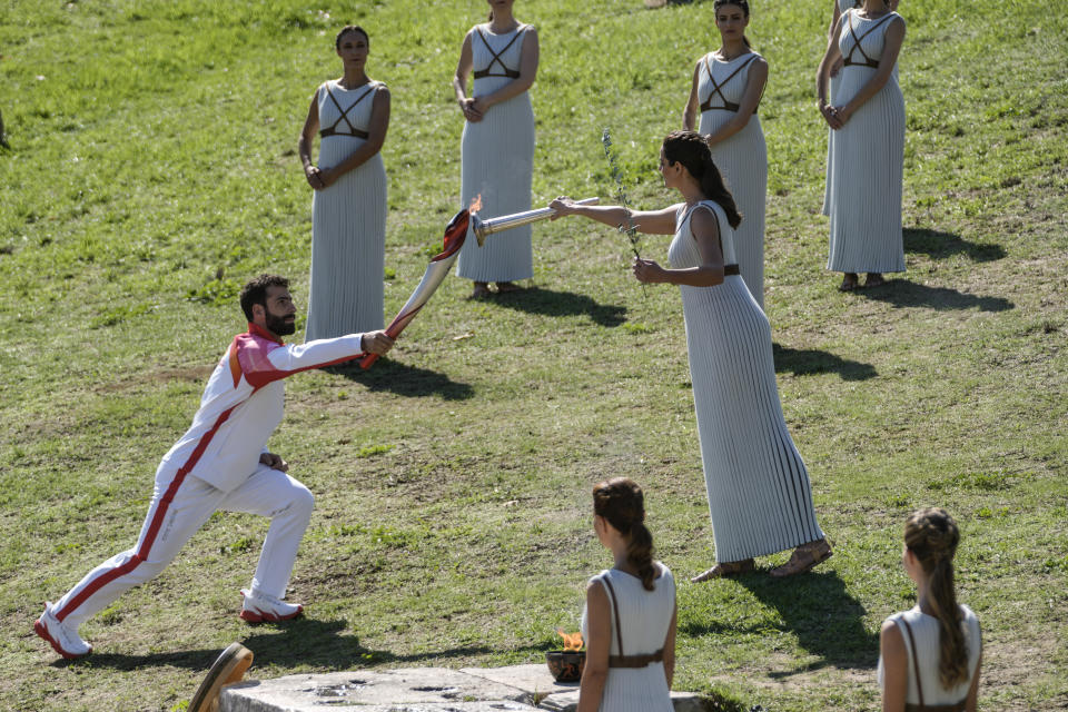 Greek actress Xanthi Georgiou, playing the role of the High Priestess, passes the flame to first torchbearer, Greek alpine ski racer Ioannis Antoniou during the lighting of the Olympic flame at Ancient Olympia site, birthplace of the ancient Olympics in southwestern Greece, Monday, Oct. 18, 2021. The flame will be transported by torch relay to Beijing, China, which will host the Feb. 4-20, 2022 Winter Olympics. (AP Photo/Petros Giannakouris)