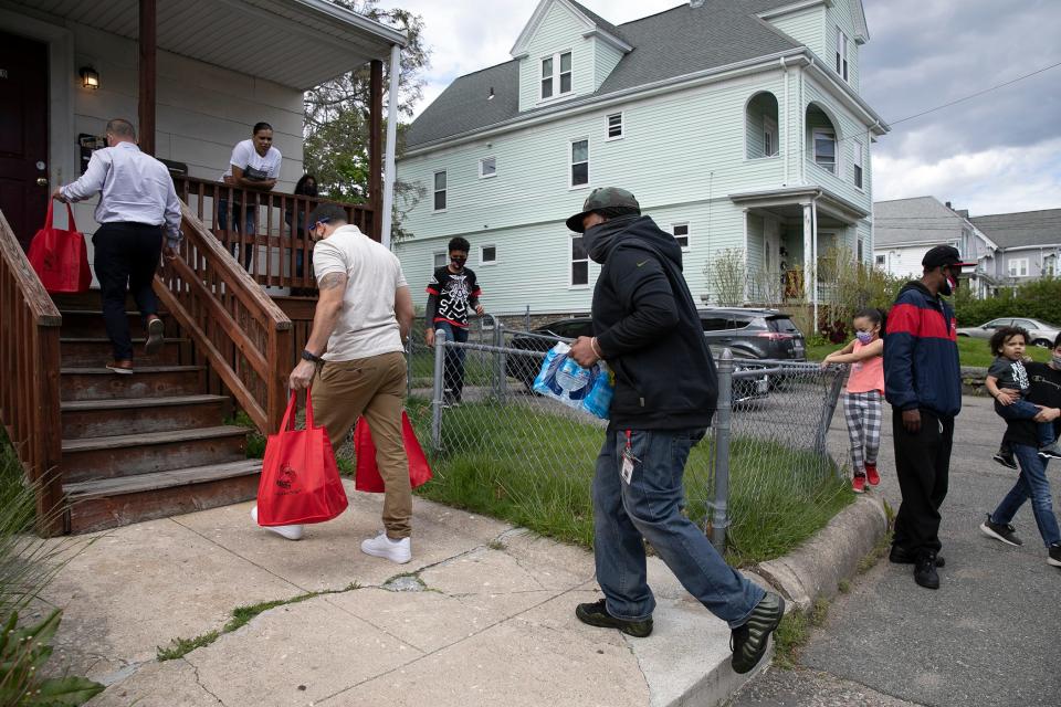 Brockton Public Schools mentors John Snelgrove, Jordan Cruz and Tristan Fortsmith carry food and water up the stairs of the Ribeiro family’s Spring Street home in Brockton on Thursday, May 13, 2021.