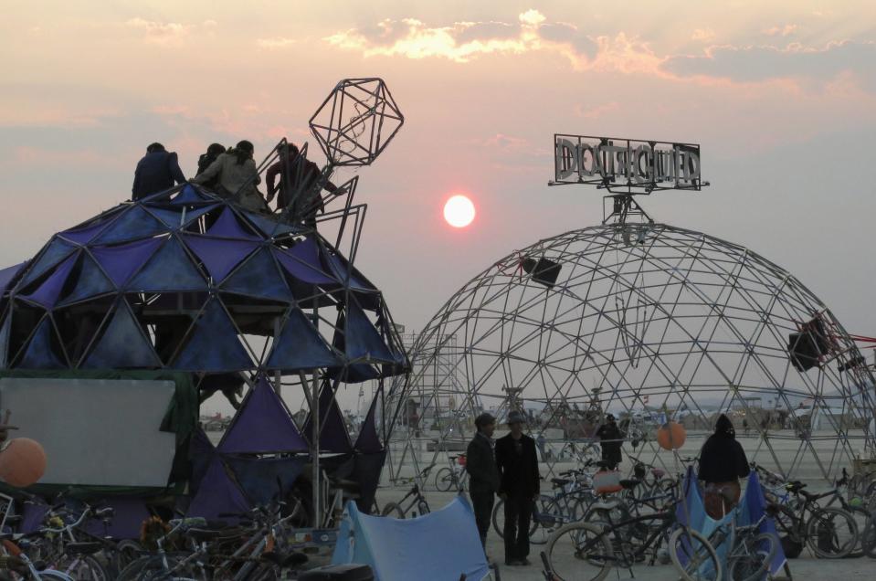 Participants watch the sunrise from the top of a dome at the 2013 Burning Man arts and music festival, in the Black Rock Desert of Nevada