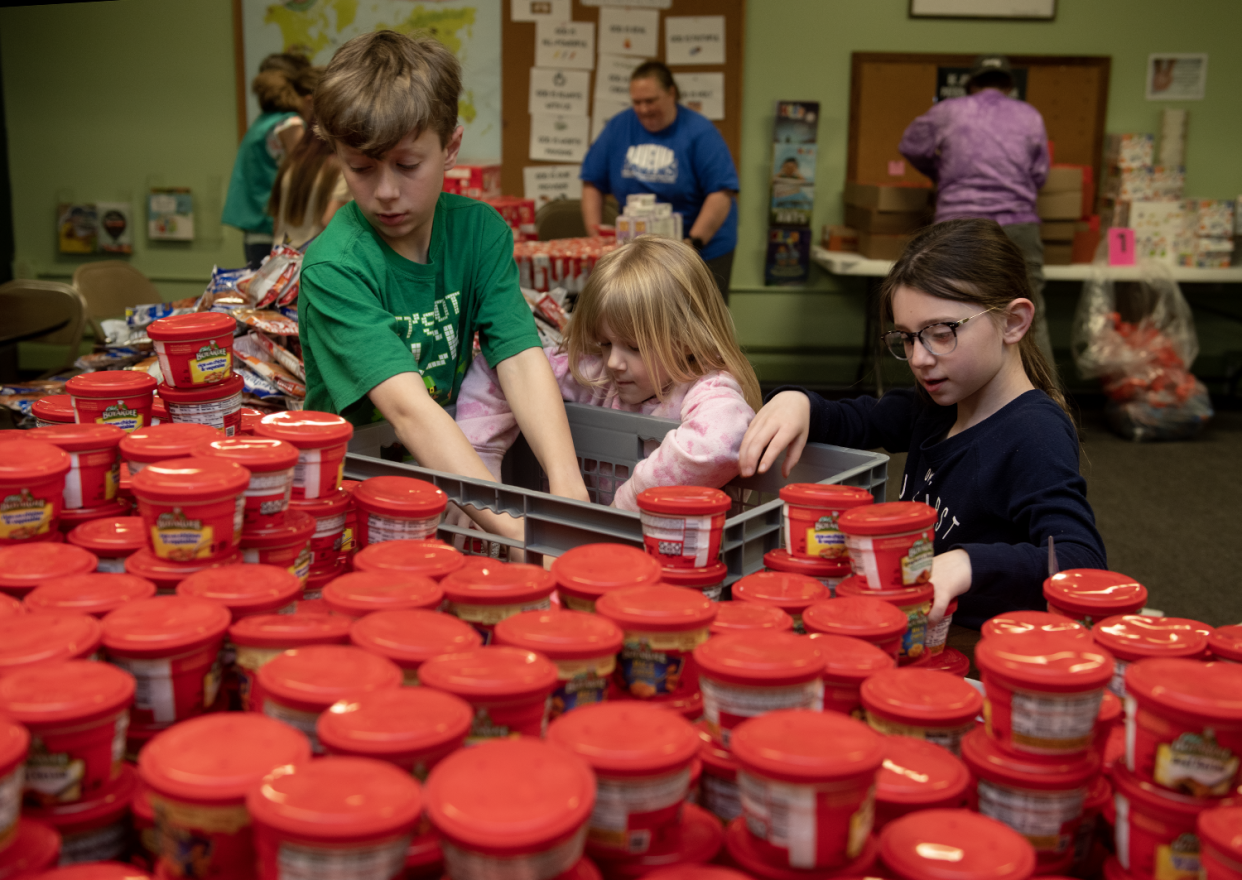 Mikey Wisniewski, 10, Lily Wisniewski, 5, and Genevieve Wisniewski, 7, unpack microwave dinners while volunteering for Raven Packs on April 27. The nonprofit provides free food for Ravenna students to take home for weekends and breaks.
