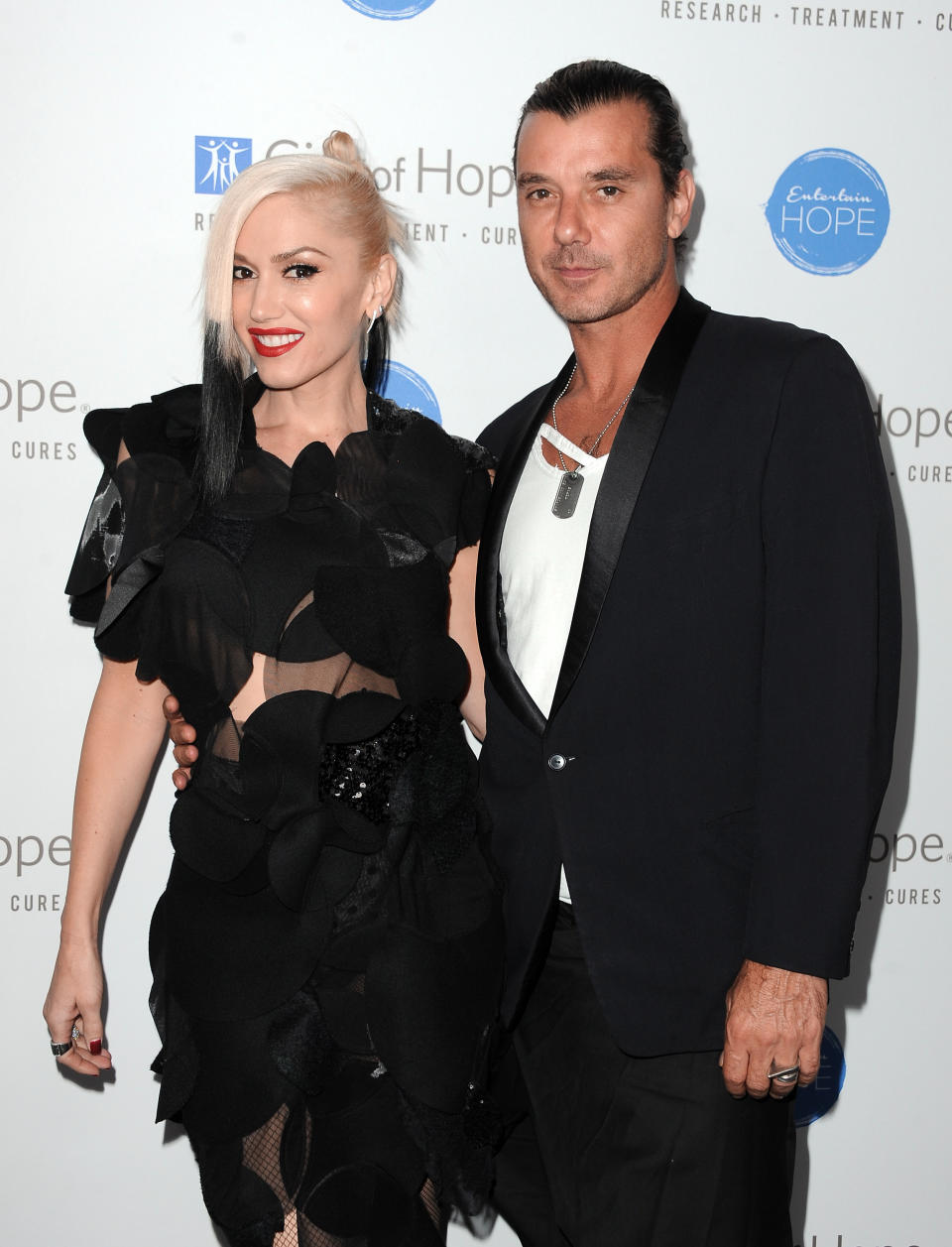 Gwen in a black ruffled outfit, and Gavin in a dark suit with a white shirt, at a media event