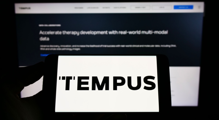 Person holding mobile phone with logo of American health care company Tempus Labs Inc. on screen in front of web page. Focus on phone display.