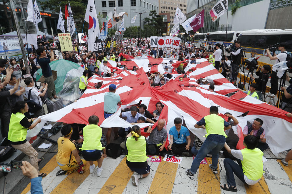 FILE - In this July 20, 2019, file photo, protesters tear a Japanese rising sun flag during a rally denouncing the Japanese government's decision on their exports to South Korea in front of Japanese Embassy in Seoul, South Korea. Japan’s “rising sun” flag is raising anger at the Olympics, with some of the host nation’s neighbors calling for it to be banned during the Tokyo Games, which start Friday, July 23, 2021. (AP Photo/Ahn Young-joon, File)