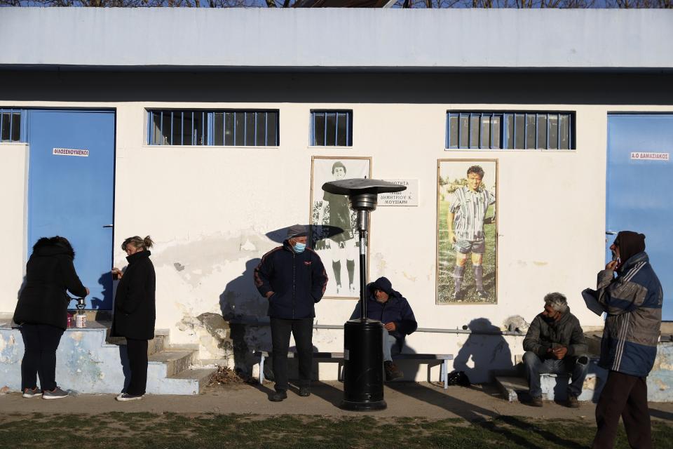 Local residents try to warm themselves in the early sunshine at a soccer field after an earthquake in Damasi village, central Greece, Thursday, March 4, 2021. Fearful of returning to their homes, some thousands of people in central Greece spent the night outdoors after a powerful earthquake Wednesday, felt across the region, damaging some homes and public buildings.(AP Photo/Vaggelis Kousioras)