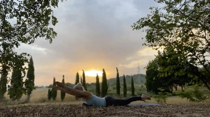 Woman practicing yoga outside on her mat with her arms alongside her ears